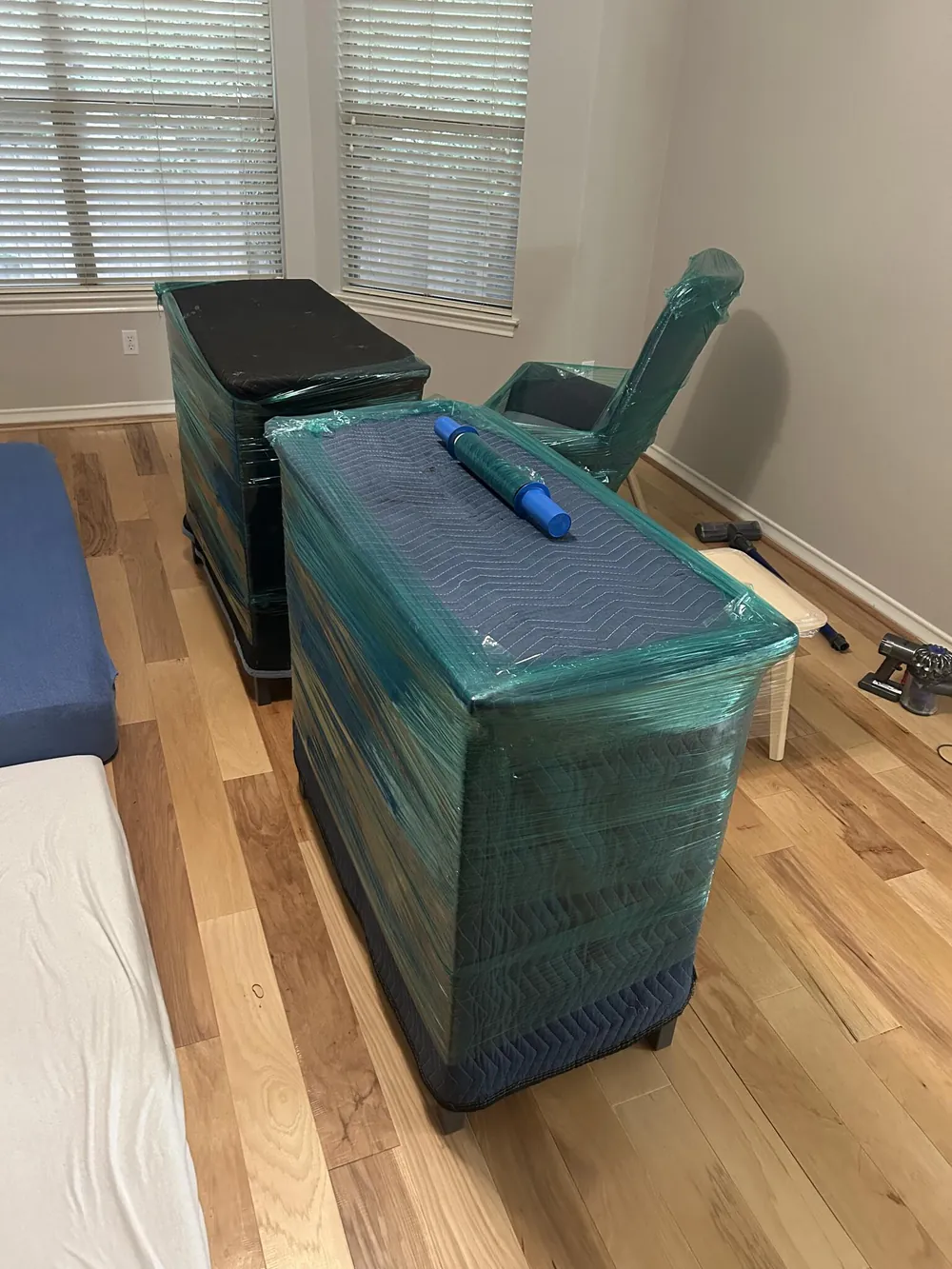 Two dressers wrapped in blue moving pads and stretch wrap in an empty room