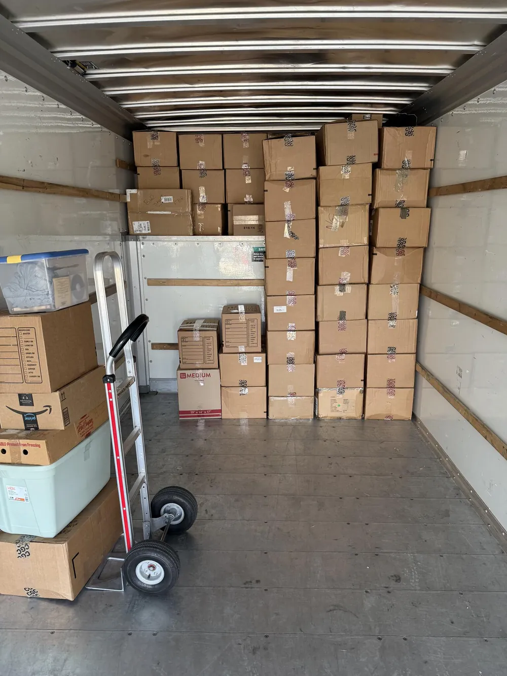 A floor-to-ceiling wall of moving boxes in a box truck, a hand truck in front