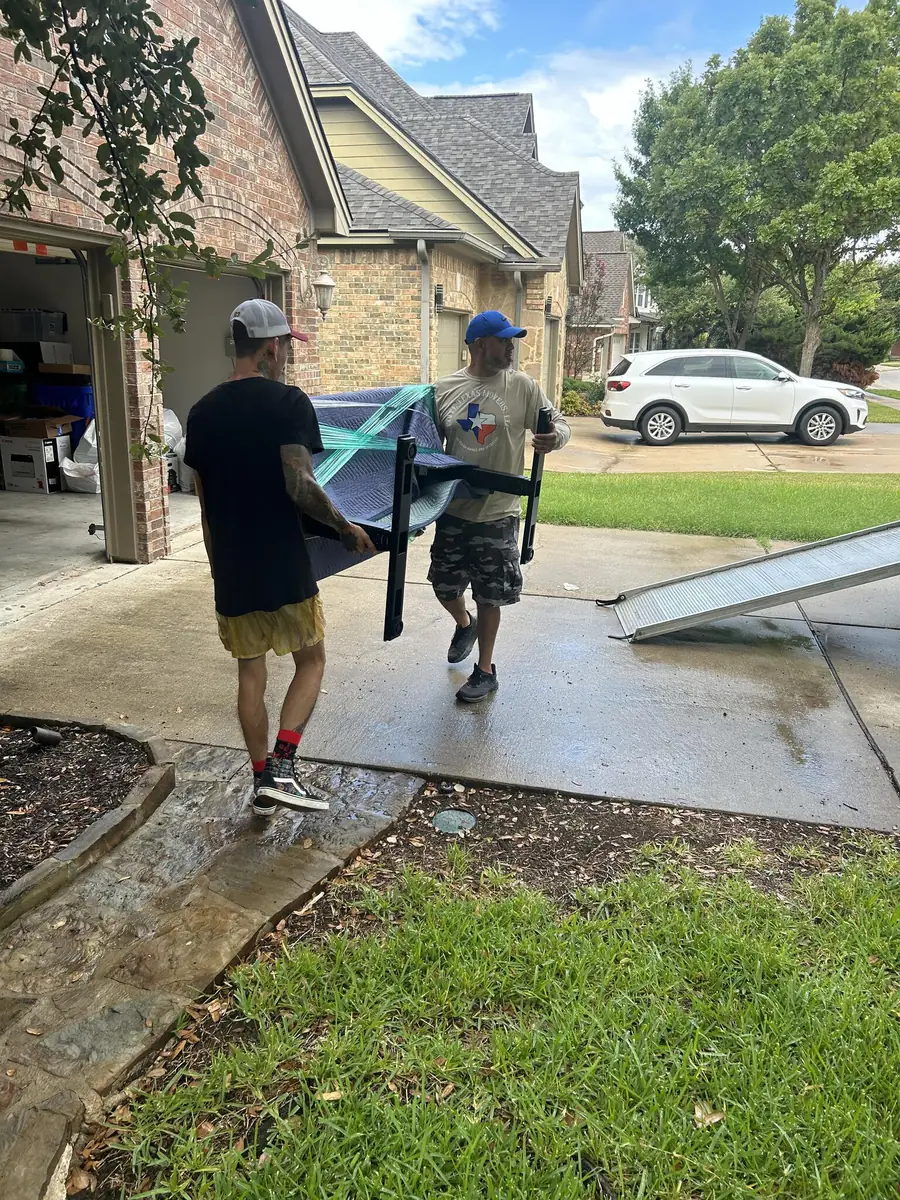 Two of the crew carry a pad-wrapped table down a driveway toward the ramp