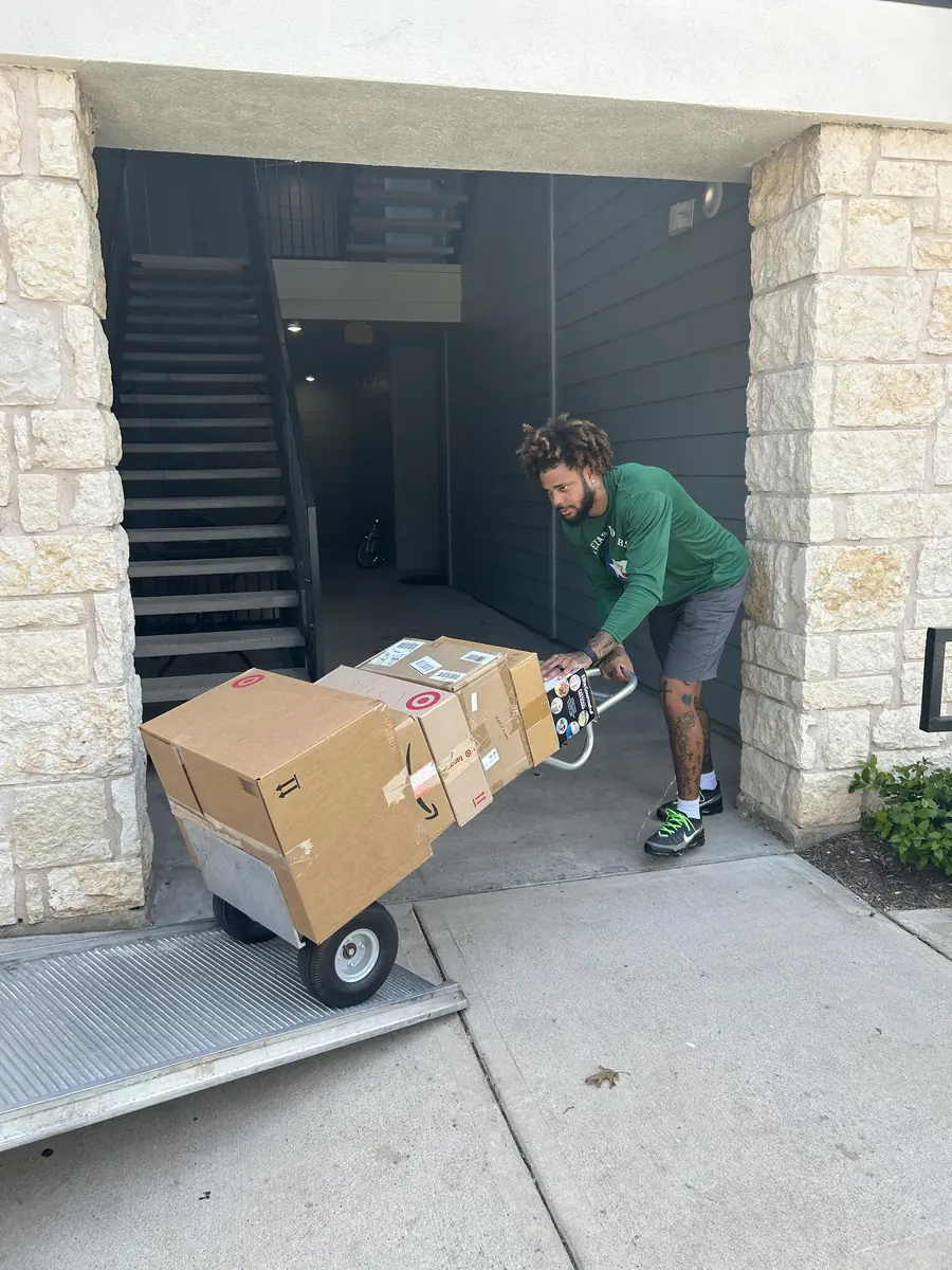 A crew member wheels a hand truck stacked with boxes out of an apartment stairwell