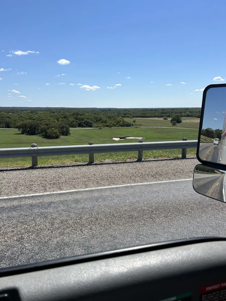 A Texas highway and green pasture seen from the cab, a mirror on the right