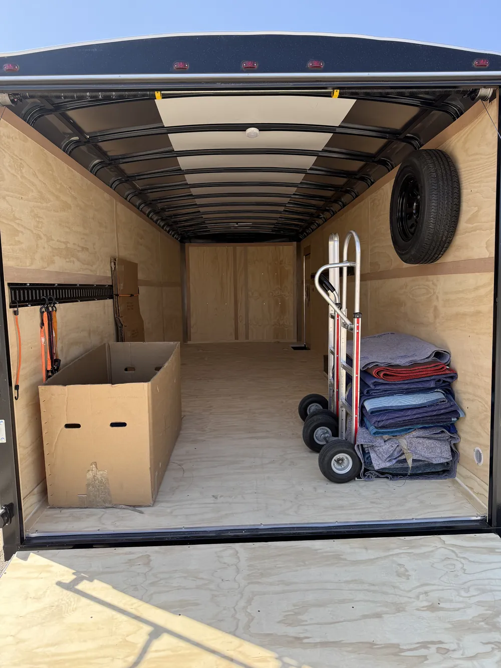 The empty trailer: plywood walls, black roof bows, hand trucks and a stack of moving pads