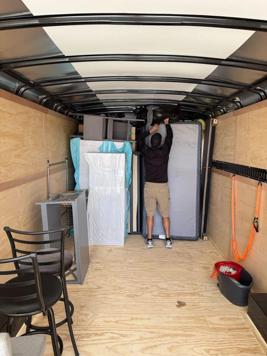 A crew member stands a mattress against the load inside the trailer, straps on the E-track