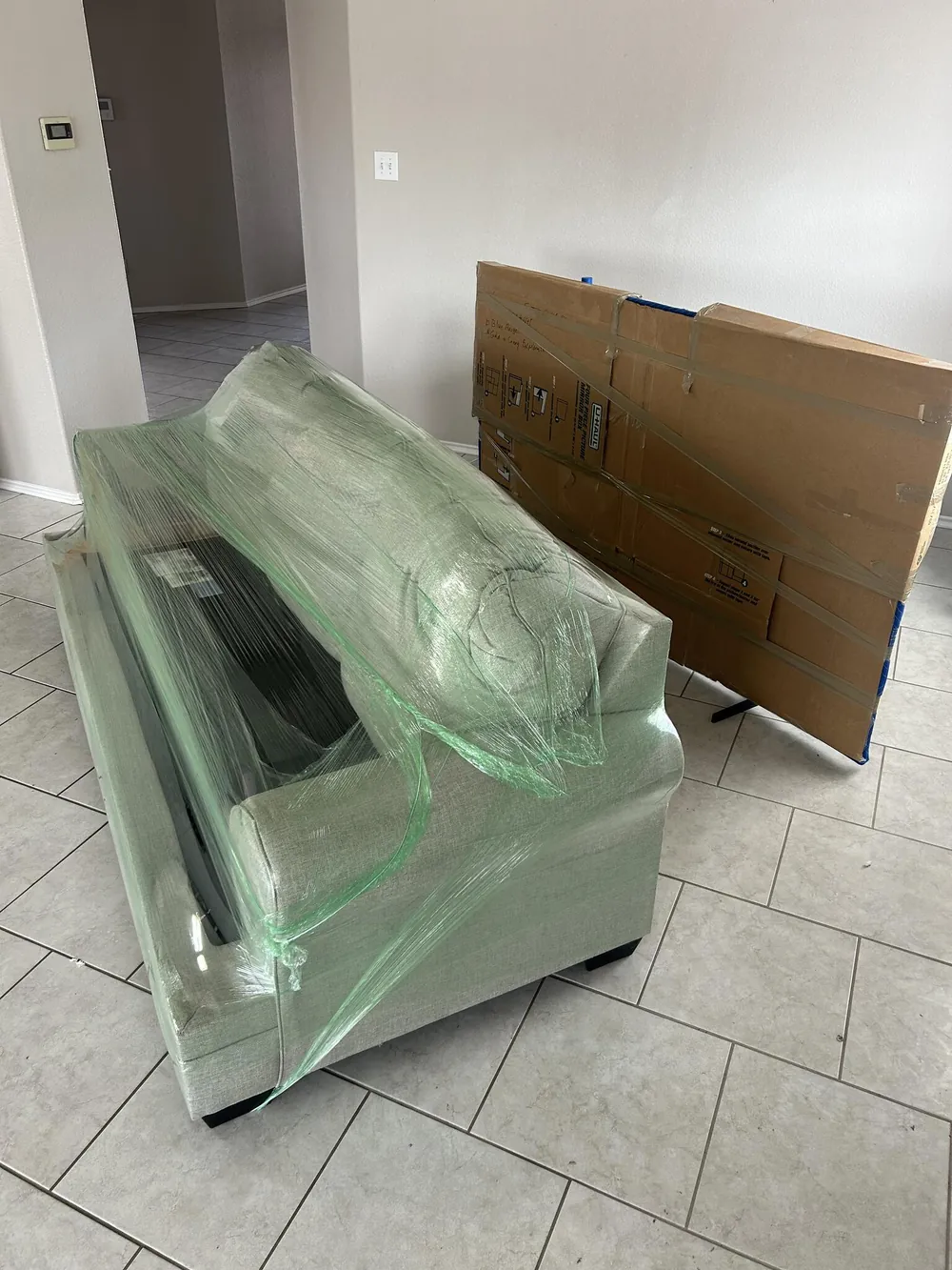 A sofa wrapped in clear plastic beside a padded table top